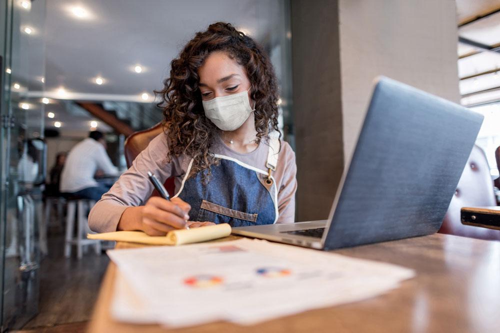A business manager doing the books at a restaurant wearing a facemask.