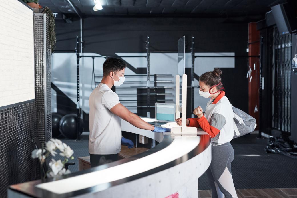 A young woman signs in at the reception desk of a gym.