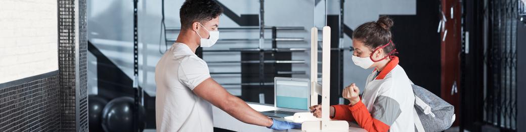 Two people standing at a reception desk who are wearing masks