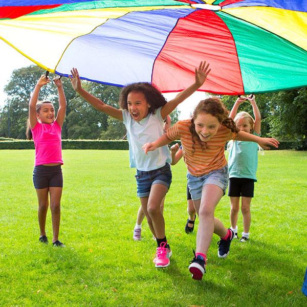 Un groupe d’enfants joue dehors, sur l’herbe, sous un parachute.