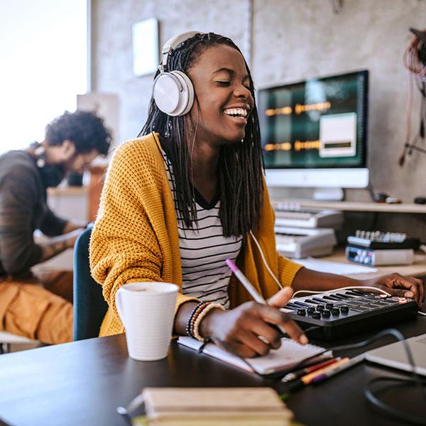 Une jeune femme noire rit en écoutant de la musique avec ses écouteurs.