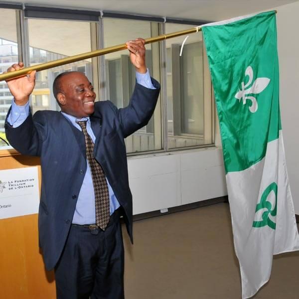 A man standing in front of a podium holds the Franco-Ontarian flag over his head.