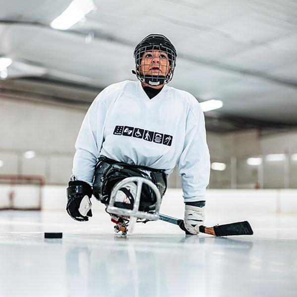 A woman plays para ice hockey in an indoor rink. 