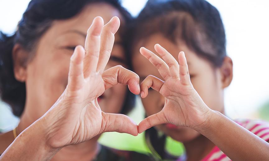 Une grand-mère et une petite fille font la forme d’un cœur en assemblant leurs mains.
