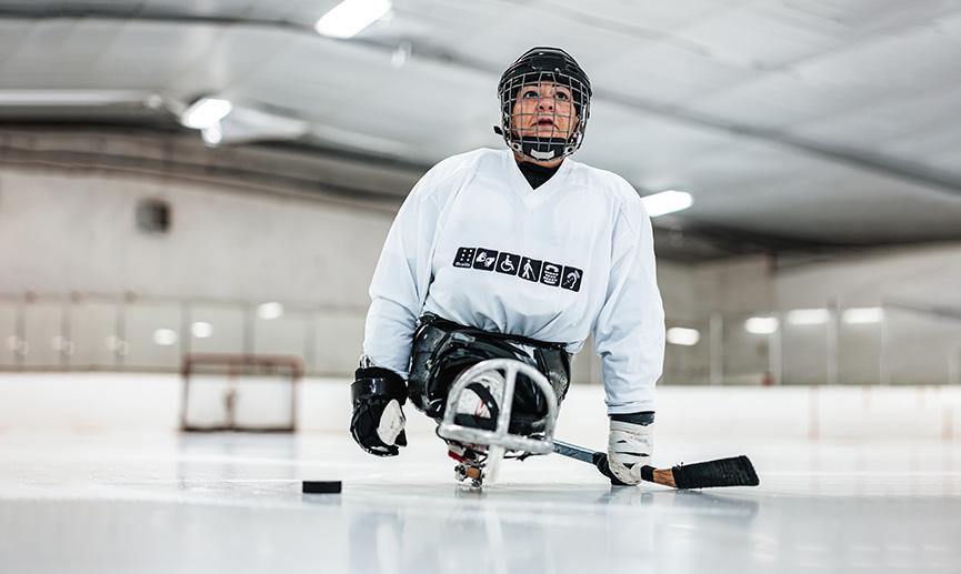 A woman plays para ice hockey in an indoor rink.