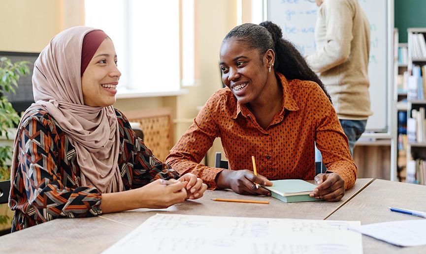 Une jeune femme noire et une du Moyen-Orient ont plaisir à parler pendant un cours.