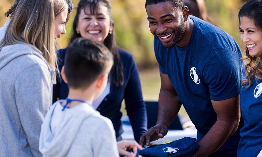 A diverse group of volunteers smile and engage with a young boy.