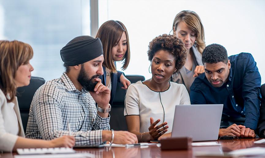 A diverse group of young adults gather around a laptop in a modern office and discuss what they see.