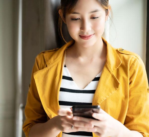 A woman is smiling as she uses her phone.