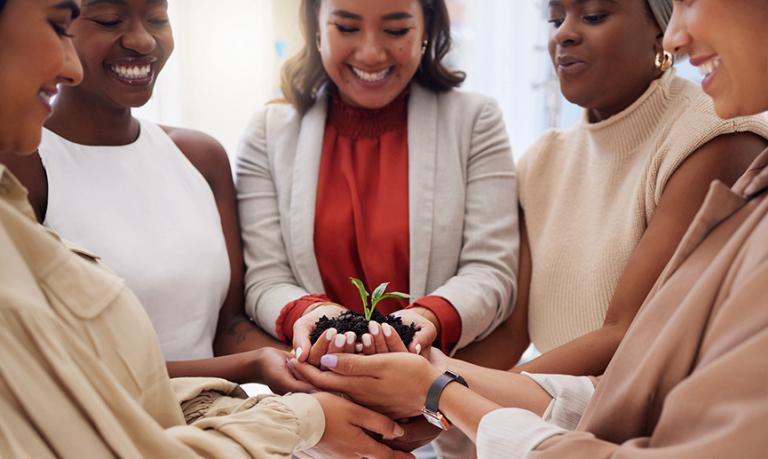 Diverse group of smiling women holding seedling in soil in hands