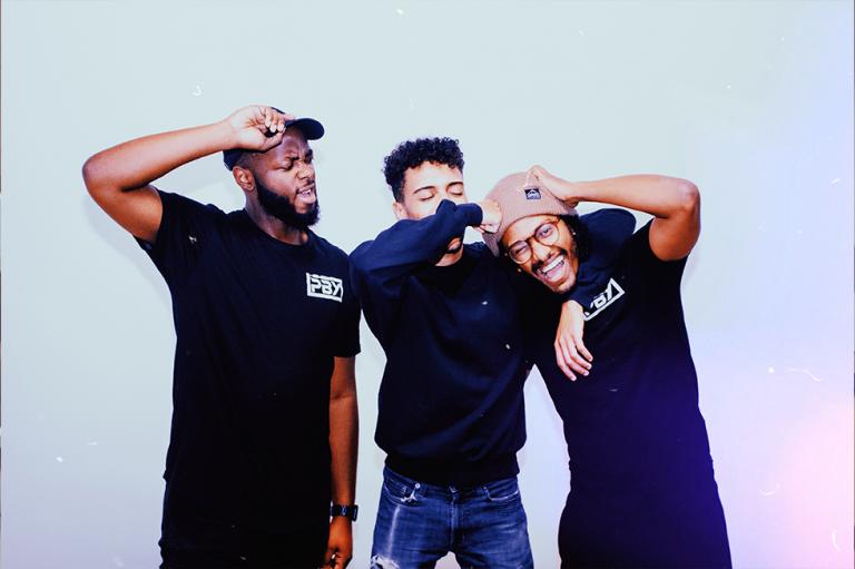 Les fondateurs de Produced by Youth, Lealem Abebe, Tafari Hall et Samuel Kanza, sont debout, souriant et riant ensemble sur un fond blanc. 