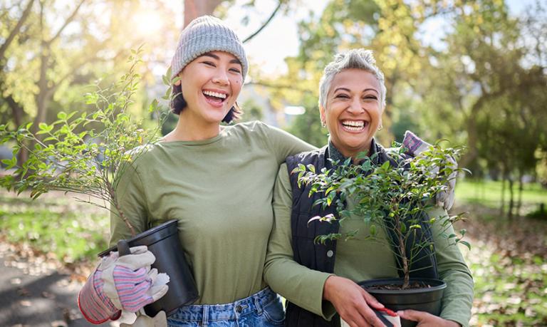 Two smiling friends are gardening in a park.