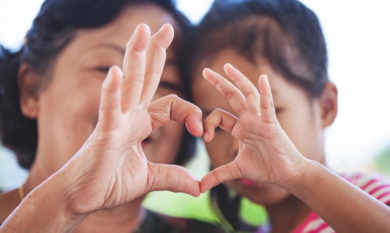 A grandmother and little child girl making heart shape with hands together.