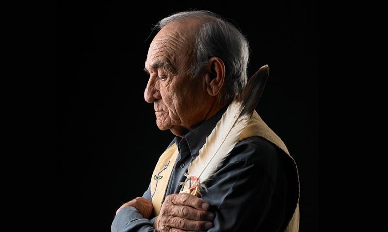 An Indigenous elder looks pensive, holding a large feather and a medicine wheel.